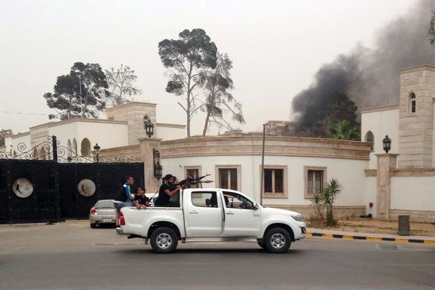 Image: Armed men aim their weapons from a vehicle as smoke rises in the background near the General National Congress in Tripoli