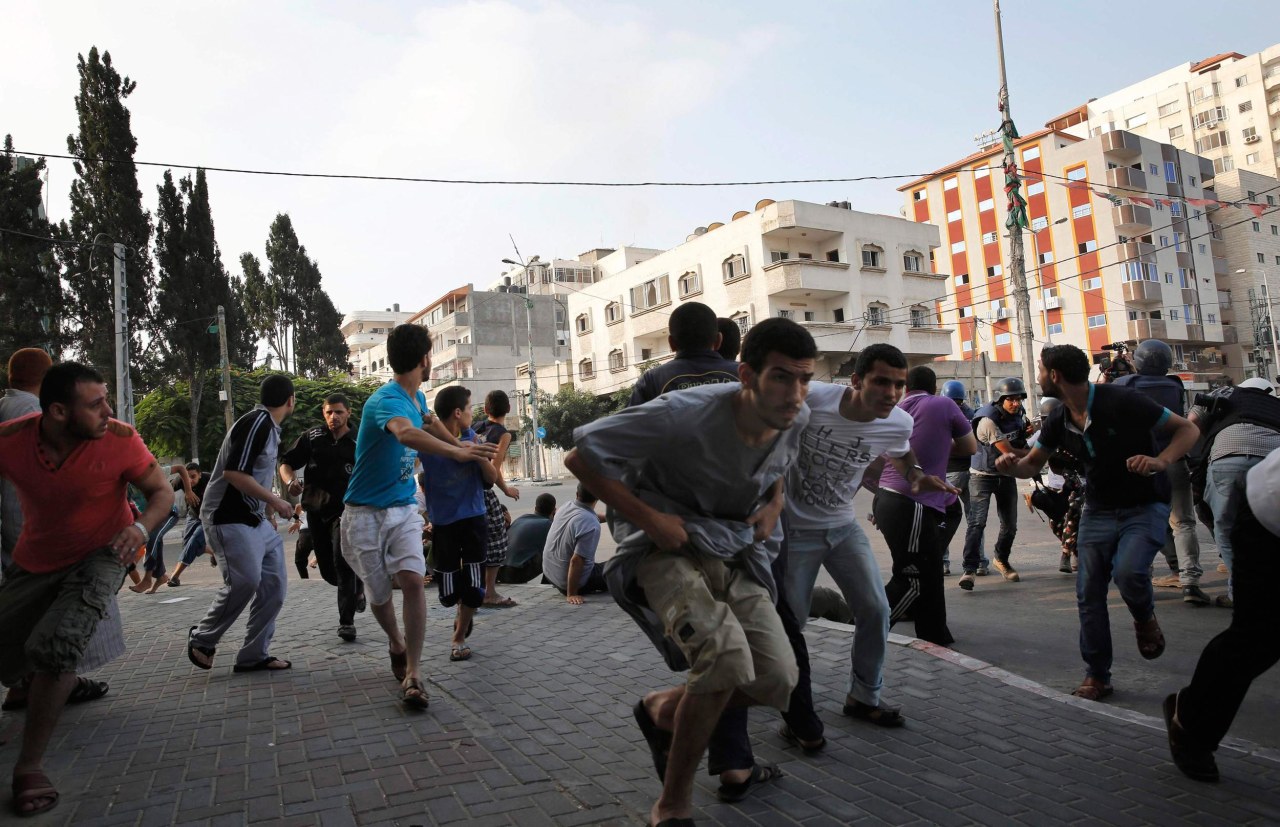 Image: Palestinians take cover as warning Israeli air strikes are fired at a nearby building in Gaza City