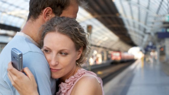 Couple embracing on station platform, woman looking at mobile phone, Separation, Horizontal, Waist Up, Indoors, Side View, Mobile Phone, Caucasian App...