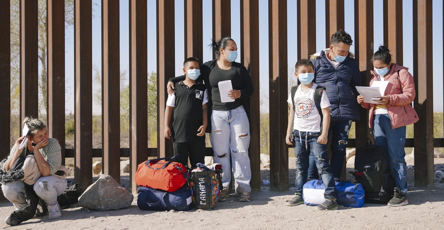 A photo of immigrants standing along the border wall