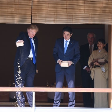 Image: Trump pours out the remaining fish food from a container as he feeds carp at a koi pond