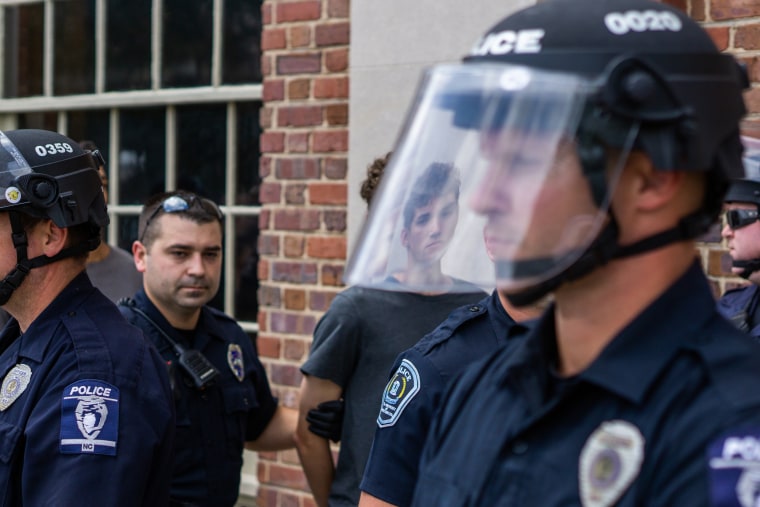 An officer leads a detained protester to a van, while other officers guard them on Aug. 25, 2018.