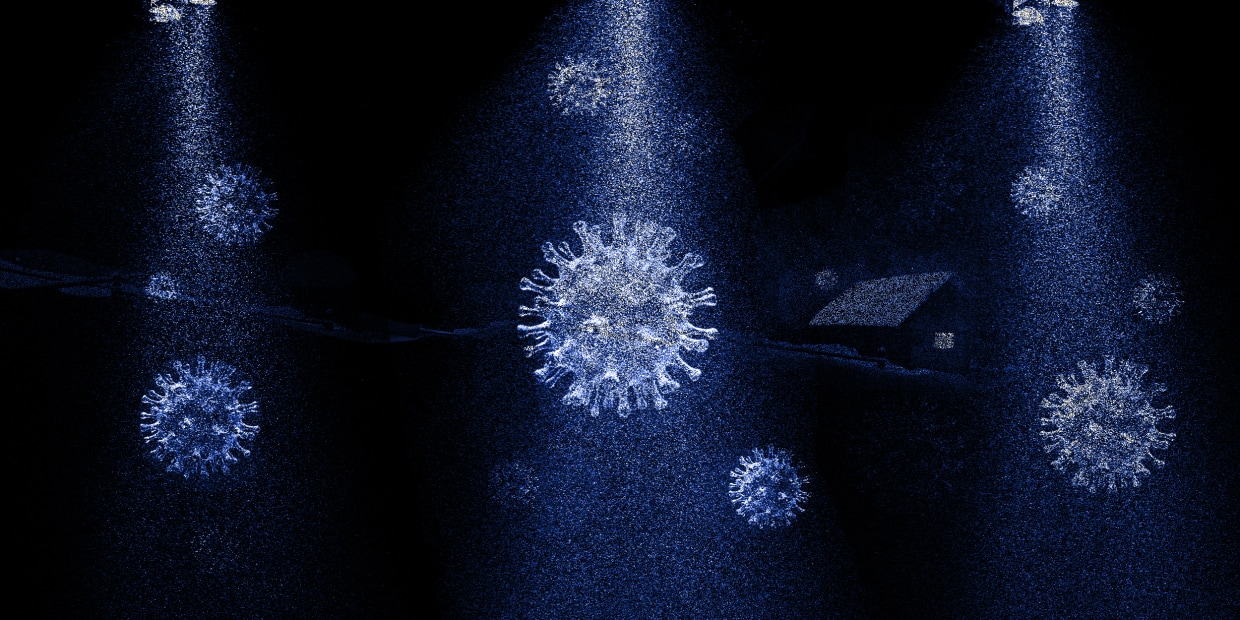 Snow falls on a nighttime scene, but the snowflakes look like coronavirus microbes. A snow-covered house with a dim light in the window sits in the background.